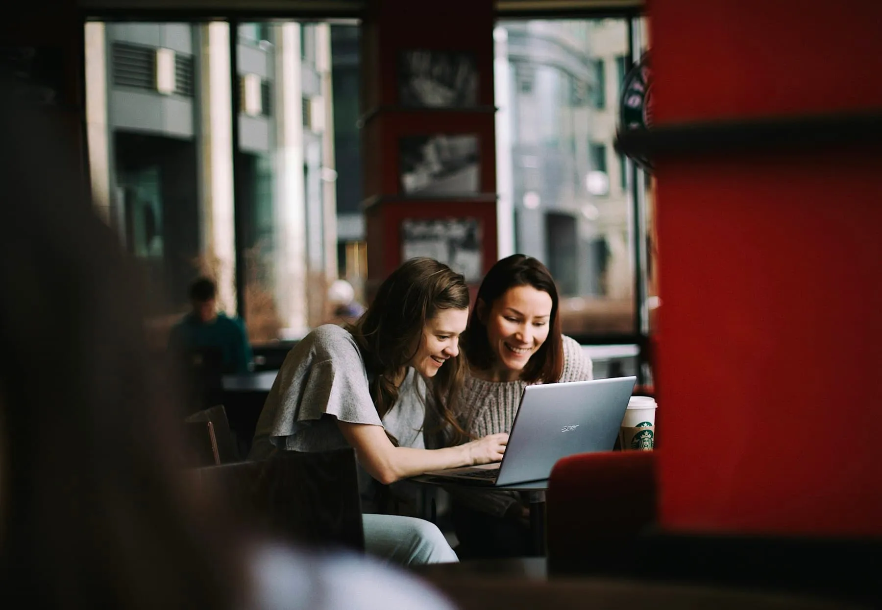 Zwei Frauen lesen gemeinsam eine Antwort auf einem Laptop in einem Café